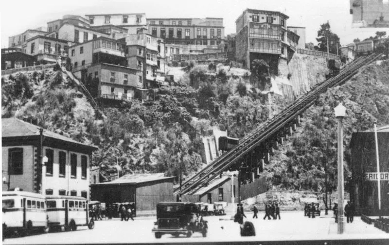 "Plaza Aduana y el Ascensor Artillería". Desde la Plaza Wheelwright en el plan (estación baja), hasta el Paseo sobre el Cerro del mismo nombre (estación alta). Es el ascensor más panorámico del puerto.  Inaugurado con dos carros el mismo año en que la Escuela Naval se instala en el edificio del cerro, 1893.